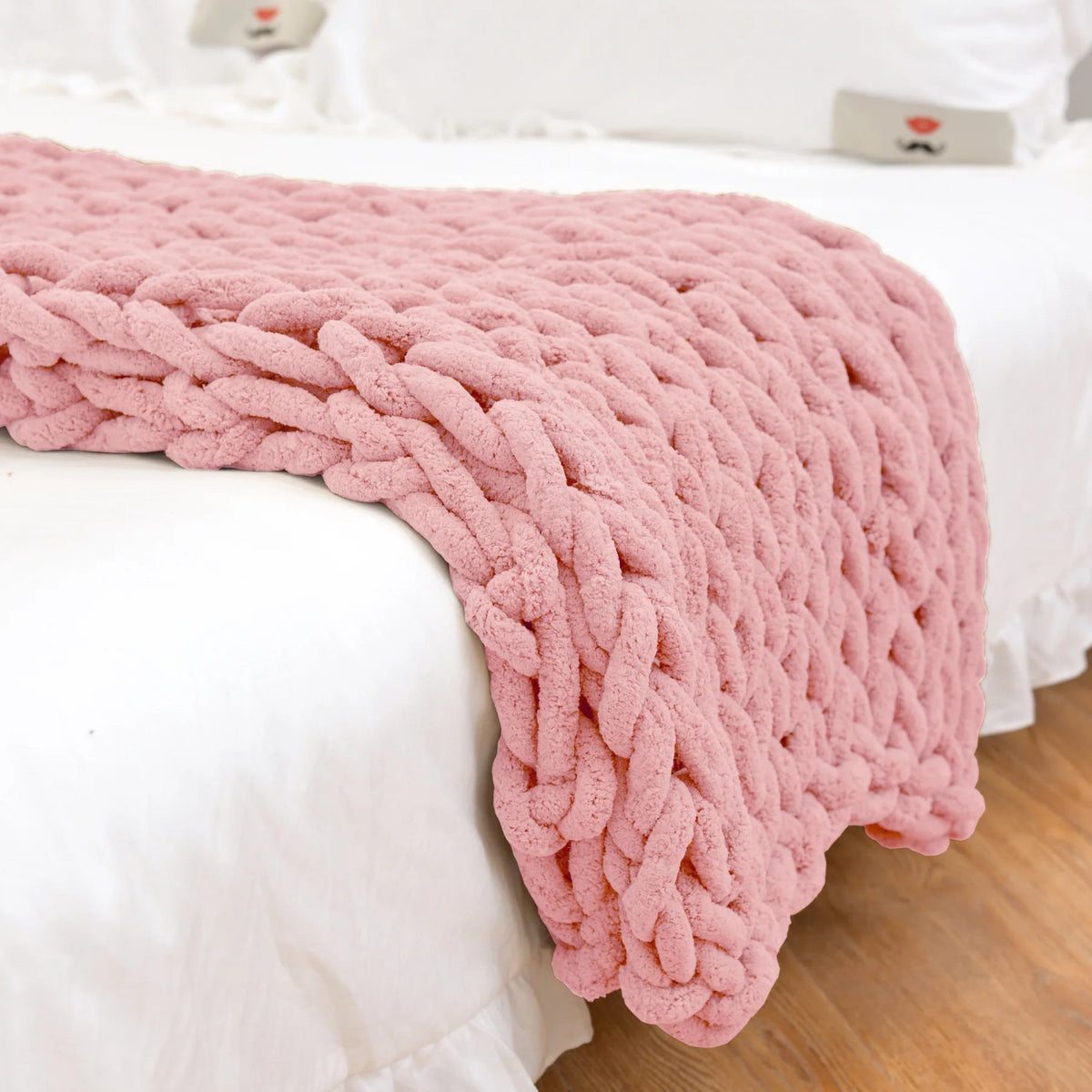 Dusty pink chunky chenille throw draped over the end of a white bed