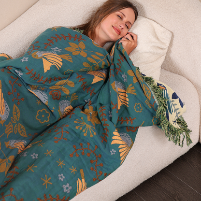 A person asleep on a cream sofa under the teal bird throw, its green fringe and a corner of the cream side at the edge