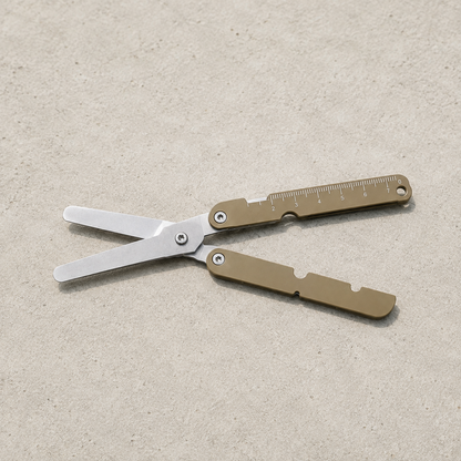 Brown folding pocket scissors open on a pale concrete surface.