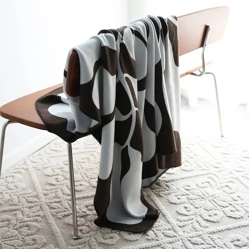 A brown and off-white knit throw blanket with an abstract pattern hung over a wooden bench.