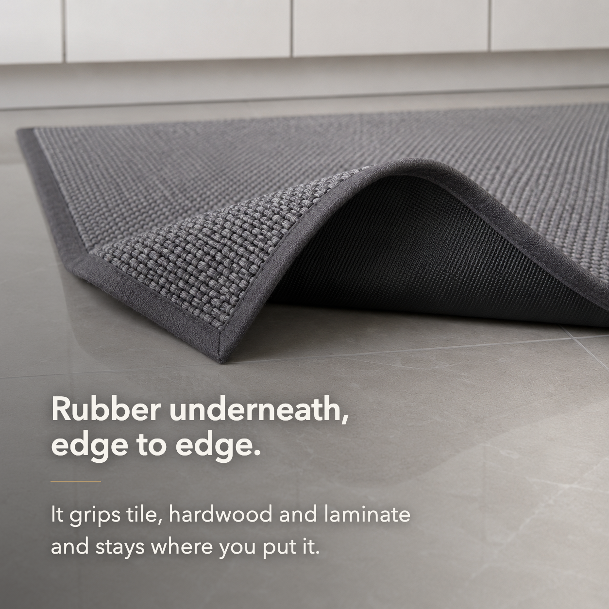 Corner of the gray woven rug turned back on tile to show the rubber backing running edge to edge