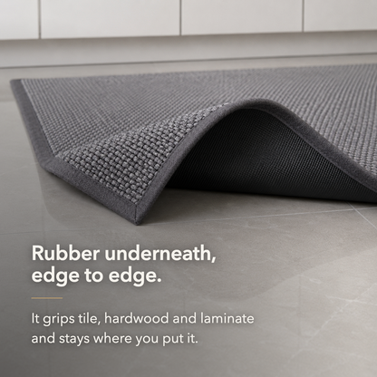 Corner of the gray woven rug turned back on tile to show the rubber backing running edge to edge