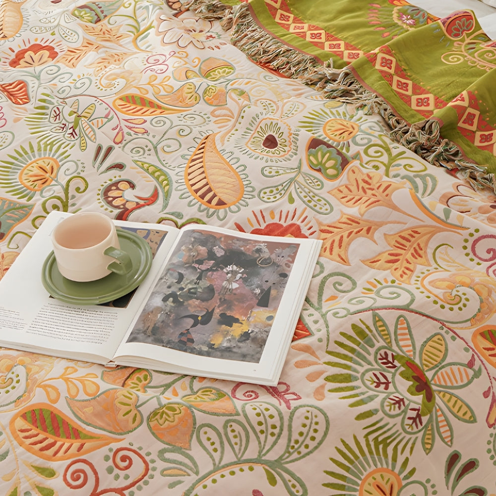A close view of the cream side of the throw, with orange and gold paisleys and leaves, an open book and a cup resting on it