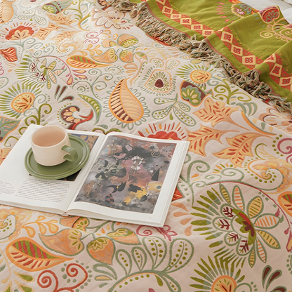 A close view of the cream side of the throw, with orange and gold paisleys and leaves, an open book and a cup resting on it