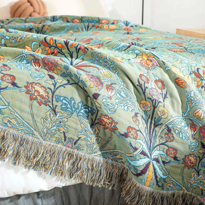 Corner of the green floral bedspread hanging over the side of a bed with its yarn fringe