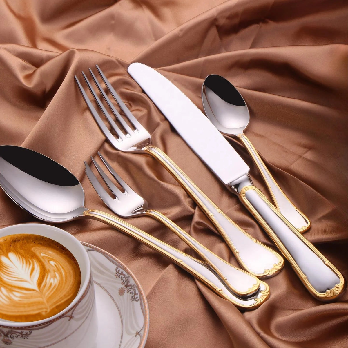 Gold trim flatware on brown satin beside a cup of coffee