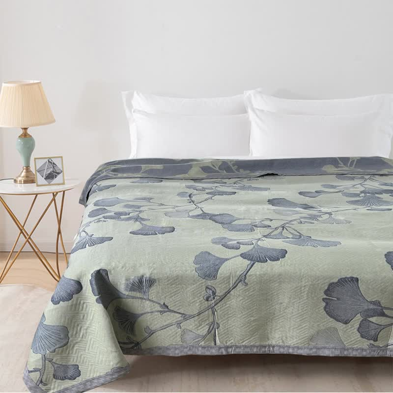 Green ginkgo leaf quilt spread over a bed with white pillows, the slate reverse showing along the top