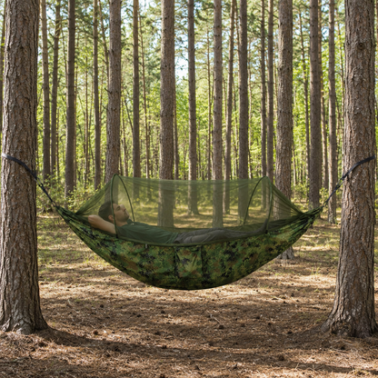 Man lying inside the closed bug net of the Camouflage Green hammock in a pine wood