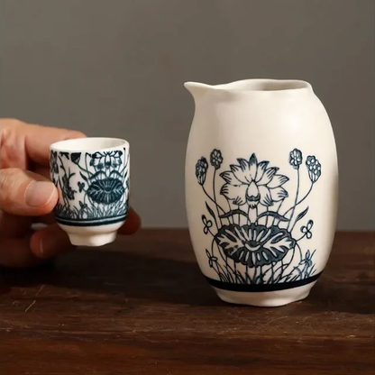A close view of the off-white decanter with its lotus drawing and pinched pouring lip, beside a lotus-pattern cup.