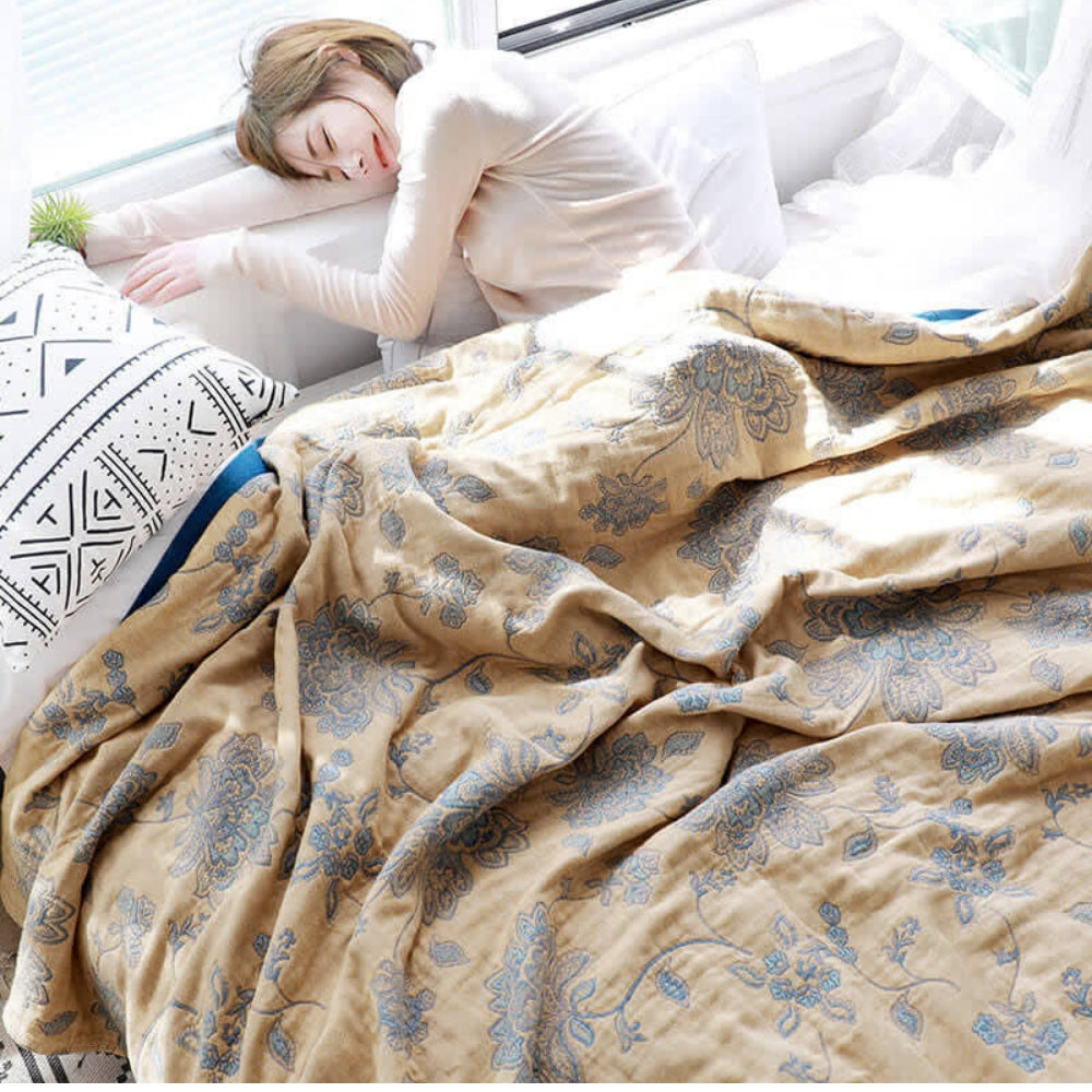 Woman asleep across a white bed under a loosely draped mustard floral jacquard blanket