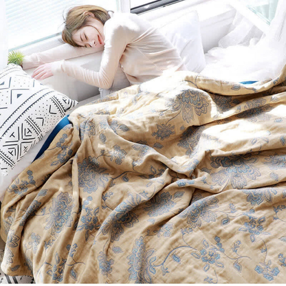 Woman asleep across a white bed under a loosely draped mustard floral jacquard blanket