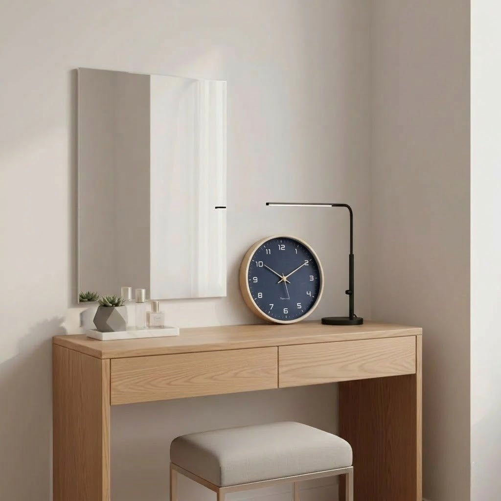 Navy blue wall clock with a pale wood frame on an oak dressing table beside a black desk lamp and a mirror