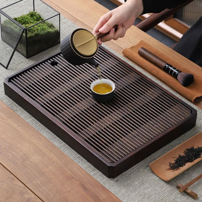 Tea poured from a side-handle pot into a small cup standing on the slats of the bamboo tea tray.