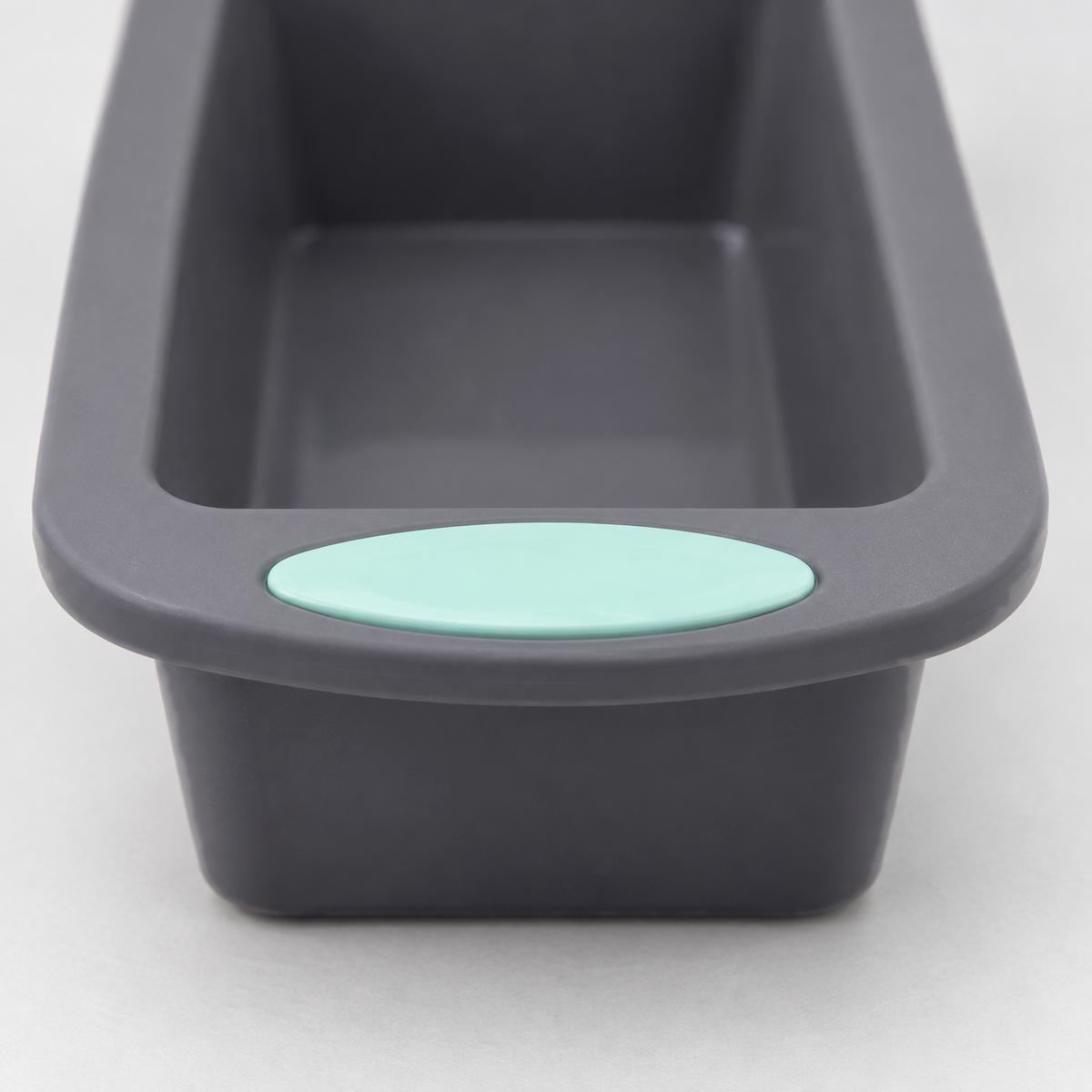 Close-up of the end of a gray silicone loaf pan showing the flush mint-green pad on its handle tab