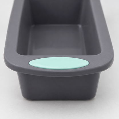 Close-up of the end of a gray silicone loaf pan showing the flush mint-green pad on its handle tab