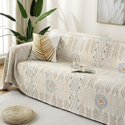 Boho blanket used as a sofa cover, cream with slate and orange sun rings, with a leaf cushion and an open book on the seat