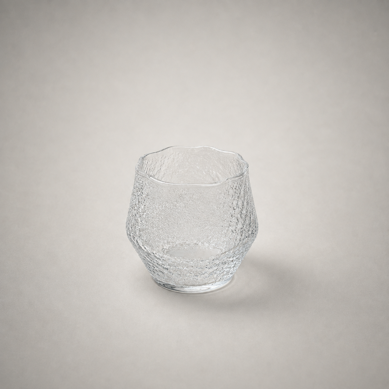 Hammered whiskey tumbler with a wavy uneven rim, shown empty on a plain grey background