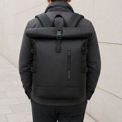Black roll top backpack worn on the back, seen from behind against a pale stone wall