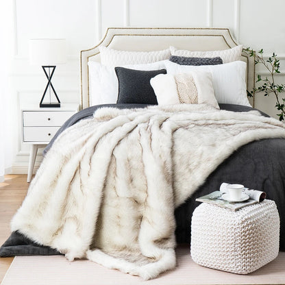 White faux fox fur throw spread over a bed with gray bedding, its long cream fur falling over the foot