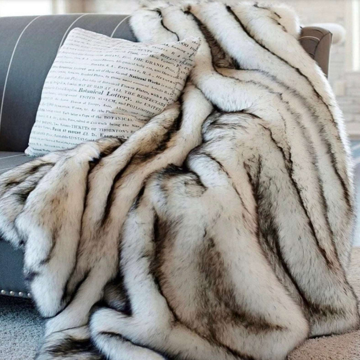 Silver faux fur throw heaped on a gray sofa beside a cushion, the black-tipped ridges running across it