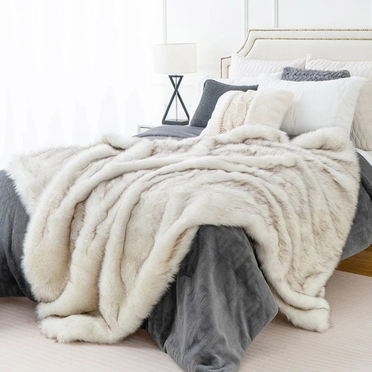 White faux fox fur throw draped over the side of a bed, the long fur falling in soft ridges