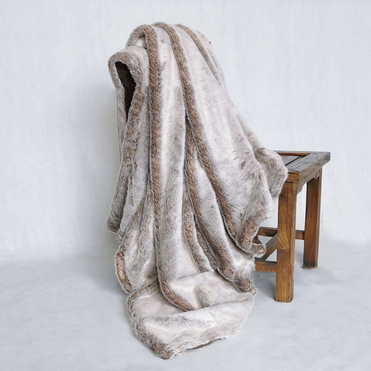 Taupe faux fur throw draped over a wooden stool, pale greige fur with brown-tipped stripes