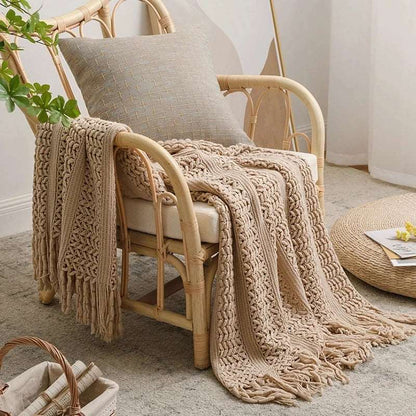 Beige crochet knit throw over a rattan armchair, one end hanging over the arm and the tassel fringe resting on a pale rug