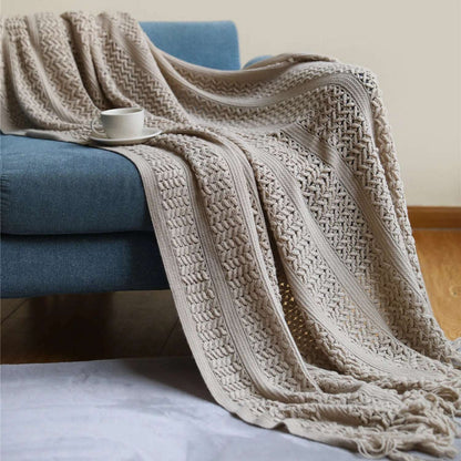 Taupe crochet knit throw draped over a blue sofa, its raised stitch stripes and open lattice falling to a tassel fringe