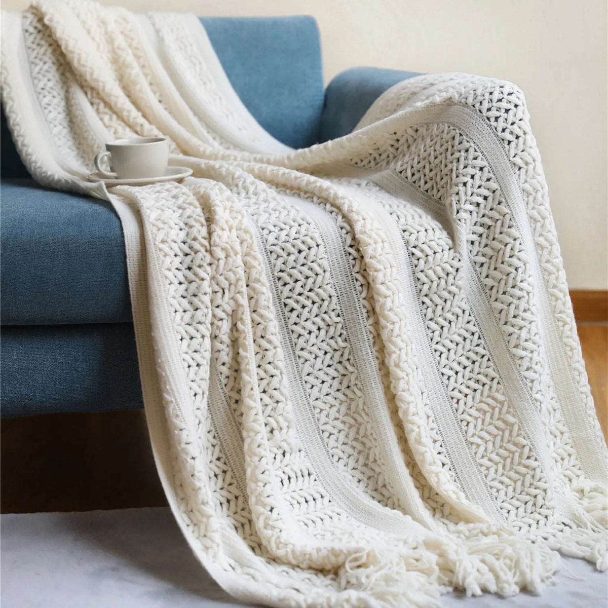 Cream crochet knit throw draped over a blue sofa, with flat knit bands between panels of raised V stitches
