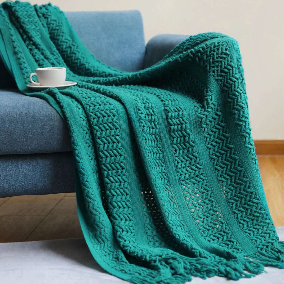 Teal crochet knit throw draped over a blue sofa, the open stitch stripes running down to a knotted tassel fringe
