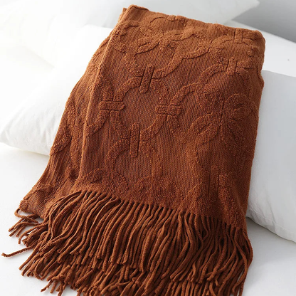 Rust jacquard knit throw folded over white pillows, the raised ring lattice and tassel fringe in burnt orange