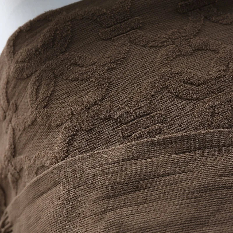 Close-up of the looped pile pattern on the brown throw beside a fold of plain ribbed knit