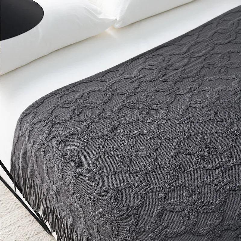 Charcoal jacquard knit throw spread over a white bed, the raised ring lattice running across it and the fringe hanging down the side
