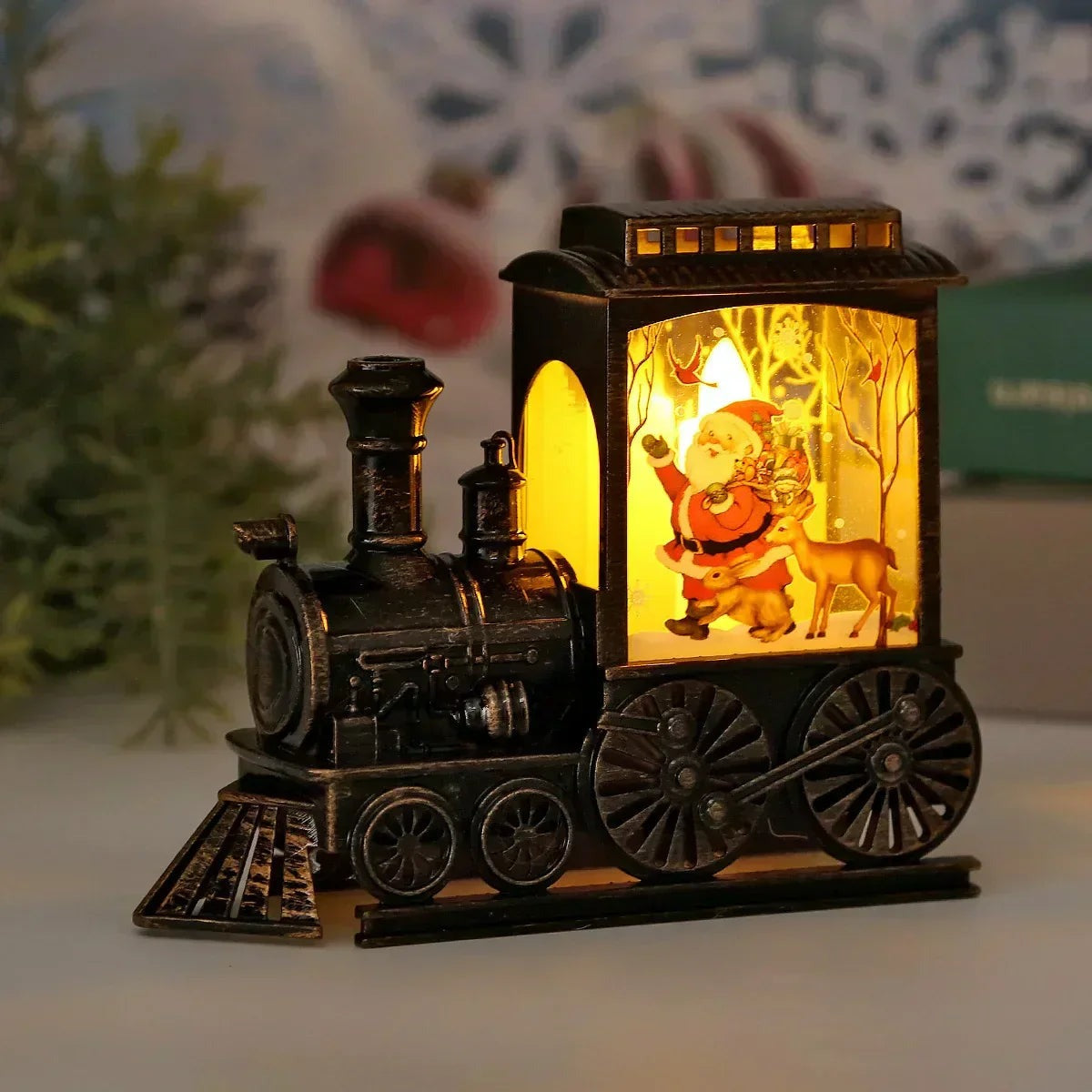 Bronze-finish train lantern glowing on a table, its cab panel showing Santa waving beside a reindeer in a snowy wood