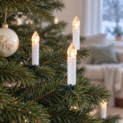 Three warm white clip-on LED candles standing upright on green clips on the branches of a fir Christmas tree in a bright living room
