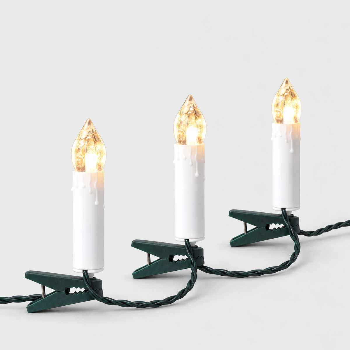 Three lit warm white clip-on LED candles standing on dark green clips, joined by one twisted green wire, on a light gray background