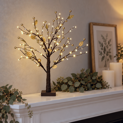 Gold tabletop twig tree glowing on a white fireplace mantel with eucalyptus greenery, pillar candles and a framed botanical print in the early evening