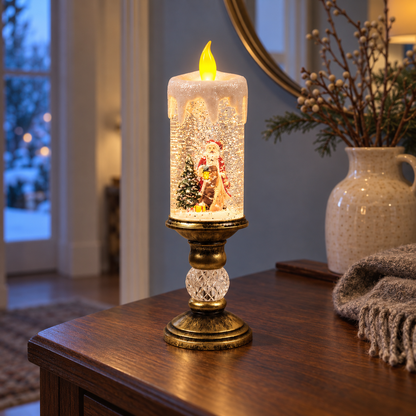 Lit snow globe candle with Santa holding a lantern beside a snowy tree, on a dark wood hallway console at dusk, next to a cream jug of berry branches and a knitted throw