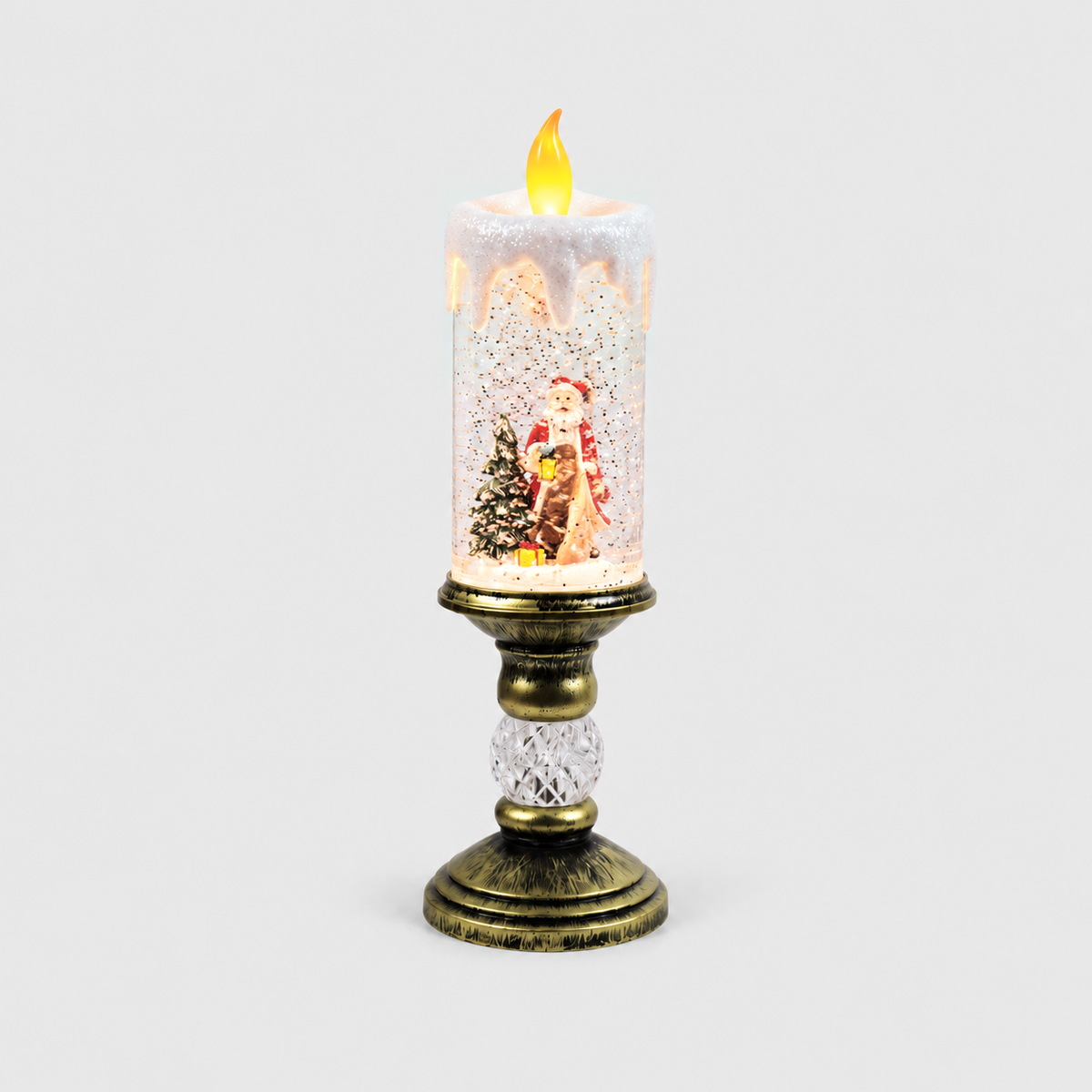 Christmas snow globe candle lit on a light gray background, Santa in a long tan robe and red coat holding a lantern beside a snowy tree inside the glittering column, on an antique gold-look pedestal