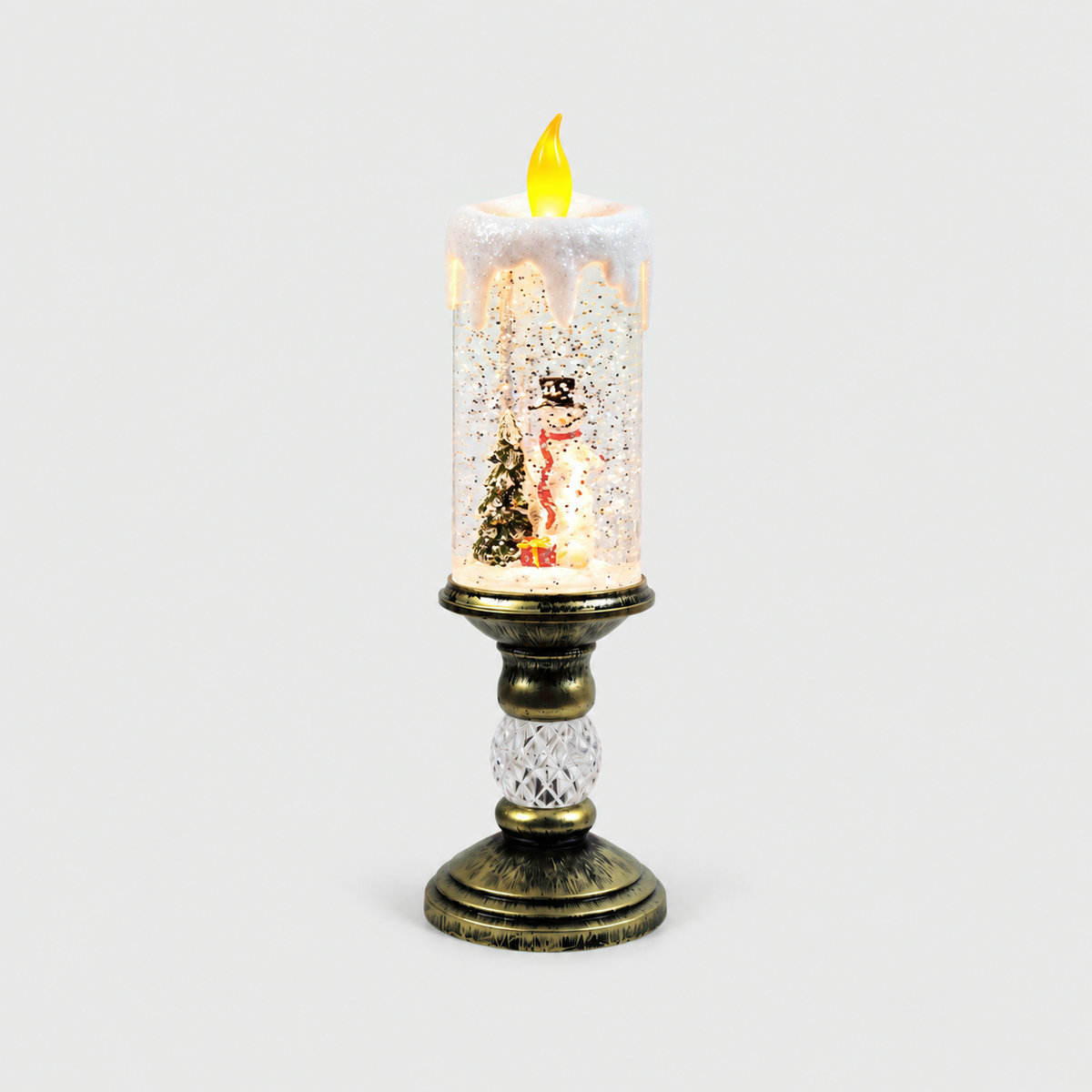 Christmas snow globe candle lit on a light gray background, a snowman in a black top hat and red scarf beside a snowy tree and a red gift inside the glittering column, on an antique gold-look pedestal