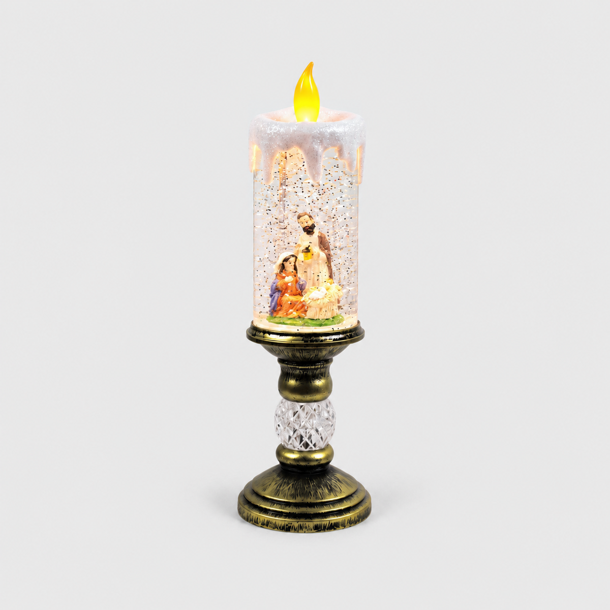 Christmas snow globe candle lit on a light gray background, the nativity scene of Mary, Joseph and the baby on a green floor inside the glittering column, on an antique gold-look pedestal