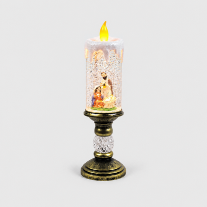 Christmas snow globe candle lit on a light gray background, the nativity scene of Mary, Joseph and the baby on a green floor inside the glittering column, on an antique gold-look pedestal