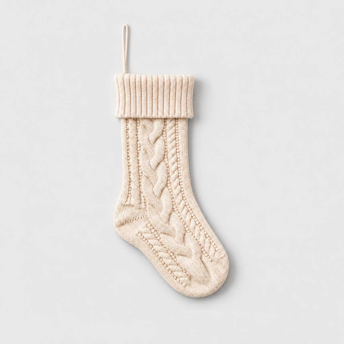 Cream cable knit Christmas stocking with a ribbed fold-over cuff and hanging loop on a light gray background