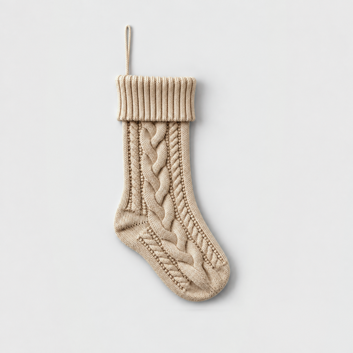 Beige cable knit Christmas stocking with a ribbed cuff on a light gray background