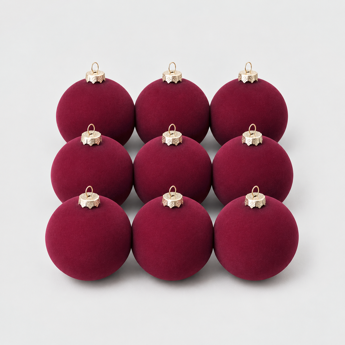 Nine burgundy velvet Christmas baubles grouped together on a light gray background