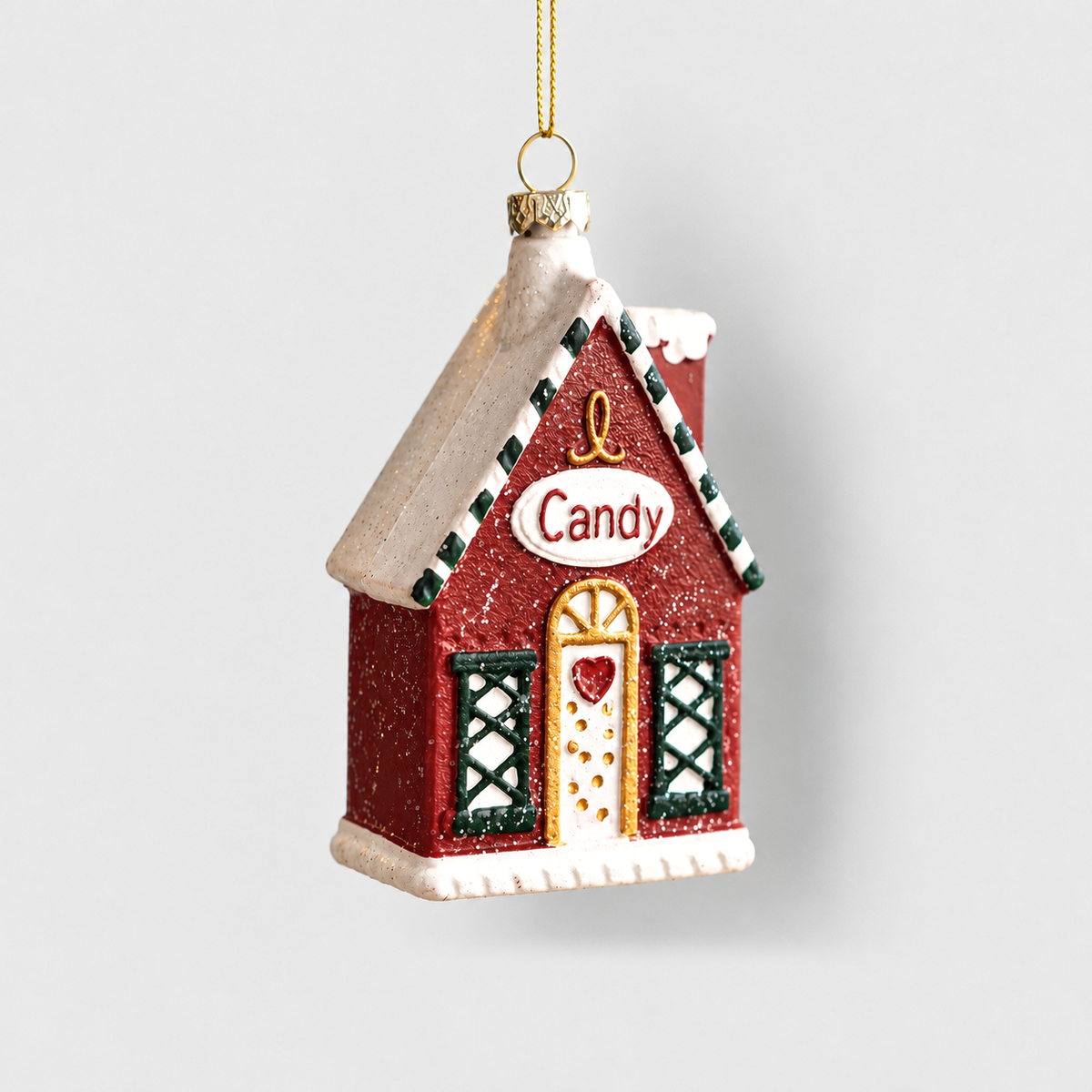 Red Christmas house ornament with a snowy roof, a Candy sign, a gold-framed door and green lattice windows, hanging from a gold cord on a light gray background