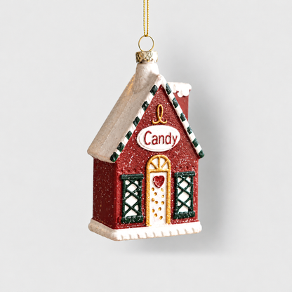 Red Christmas house ornament with a snowy roof, a Candy sign, a gold-framed door and green lattice windows, hanging from a gold cord on a light gray background