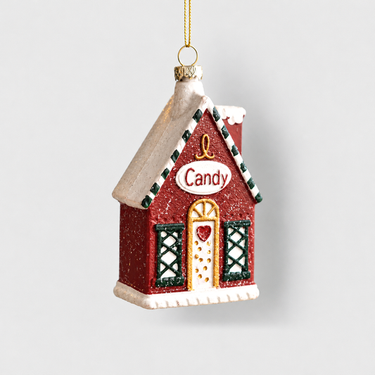 Red Christmas house ornament with a snowy roof, a Candy sign, a gold-framed door and green lattice windows, hanging from a gold cord on a light gray background