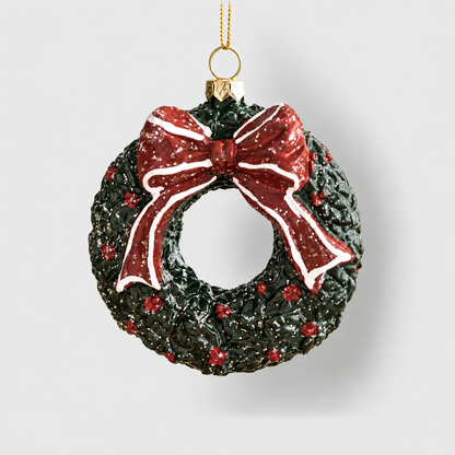 Dark green Christmas wreath ornament with red berries and a red bow, hanging from a gold cord on a light gray background