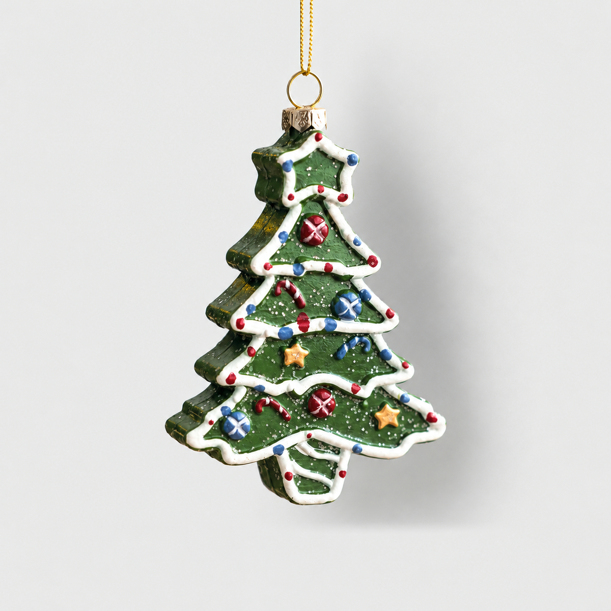 Green Christmas tree ornament with white icing piping, painted baubles and gold stars, hanging on a light gray background